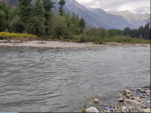 a river with rocks and trees and mountains in the background at Kumrat Glamping Resorts in Tāl