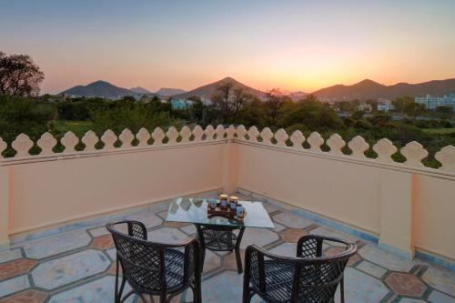 einen Balkon mit einem Tisch und Stühlen sowie Blick auf den Sonnenuntergang in der Unterkunft Udaikot by StayVista, A hill-view villa adorned with Heritage decor, Offering a terrace, Lawn & Indoor games for a perfect retreat in Udaipur
