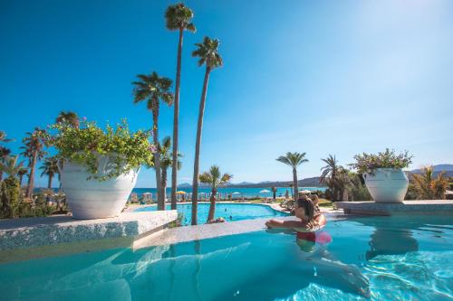 a woman sitting in a swimming pool with palm trees at Hotel Club Saraceno - Bovis Hotels in Àrbatax