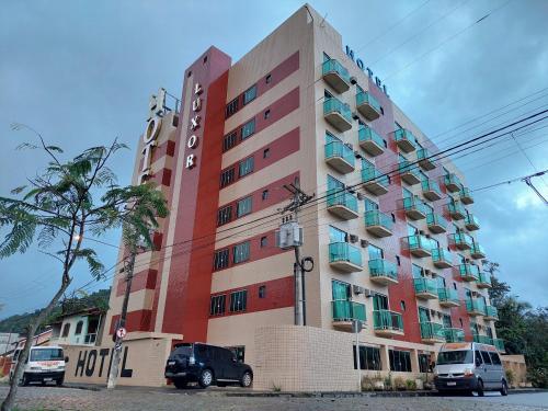um edifício alto com carros estacionados em frente em LUXOR VEROLME HOTEL em Angra dos Reis