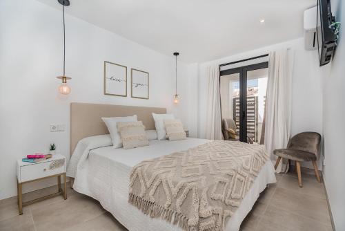 a white bedroom with a bed and a chair at Cana Ferrera in Port de Pollensa
