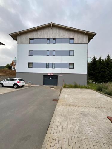 a large white building with a car parked in a parking lot at Útulný jednopokojový apartmán v alpském stylu na Klínovci in Loučná pod Klínovcem