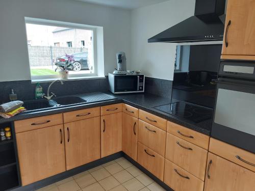 cocina con armarios de madera, fregadero y ventana en Au Chant des Oiseaux en Tournai