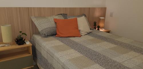 a bed with an orange pillow on top of it at Em Capao da Canoa - Luxo e conforto com praia , sol e mar em Capão. in Capão da Canoa
