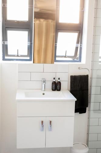 a white bathroom with a sink and two windows at Blaauw Cottage in Riebeek-Kasteel