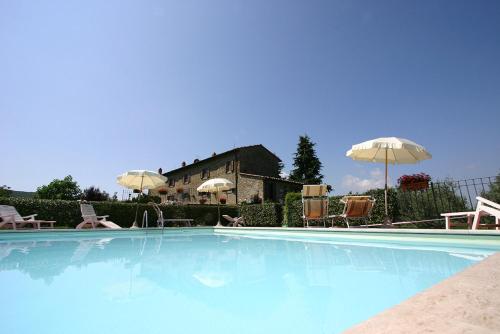 a swimming pool with chairs and umbrellas and a house at Agriturismo Cortoreggio in Cortona