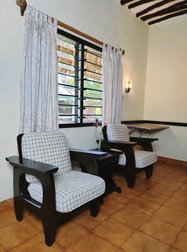 a living room with two chairs and a table and a window at Upani in Diani in Diani Beach