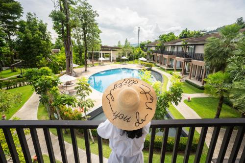 a woman wearing a hat standing on a balcony looking at a pool at The Leaf on The Sands by Katathani - SHA Extra Plus in Khao Lak