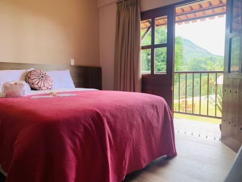 a bedroom with a bed with a red blanket and a window at Flor de Café Pousada in Pedra Menina