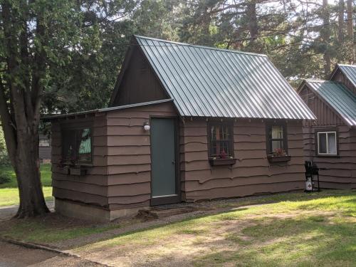 una pequeña casa con una puerta gris y un árbol en Moreno's Cottages en Saranac Lake