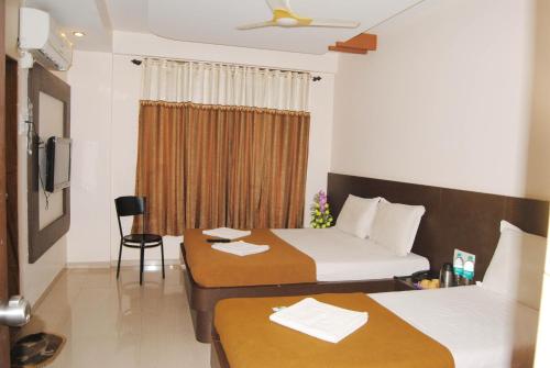a hotel room with two beds and a chair at Hotel Krishna Sai Kutir in Shirdi