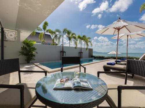 a table with a book on it next to a pool at Skye Beach Hotel - Koh Samui in Choeng Mon Beach