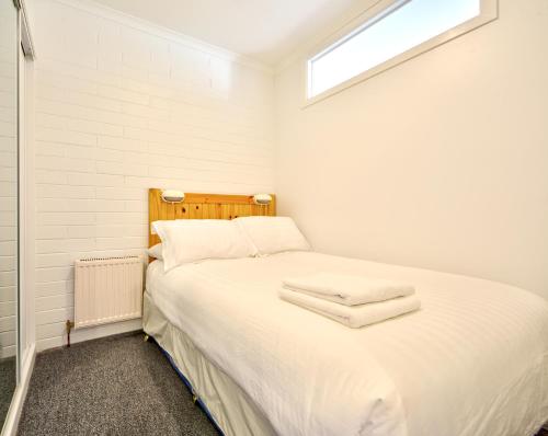 1 dormitorio con 1 cama con sábanas blancas y ventana en Snow Ski Apartments 28, en Falls Creek