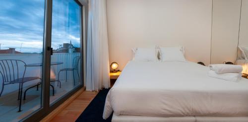 a bedroom with a large white bed and a balcony at Cravo’s Heritage House in Pinhel