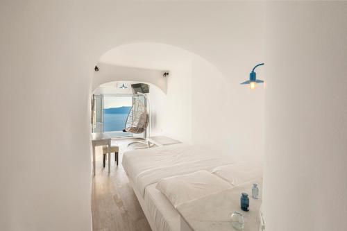 a white bedroom with a bed and a mirror at Pearl on the Cliff Hotel & Suites by Pearl Hotel Collection in Imerovigli