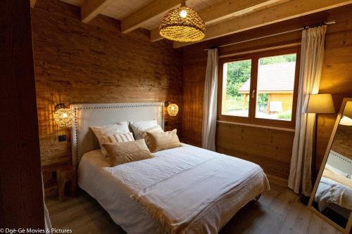 1 dormitorio con cama, ventana y lámpara de araña en Les Jardins du Hérisson Chalet 2, en Bonlieu