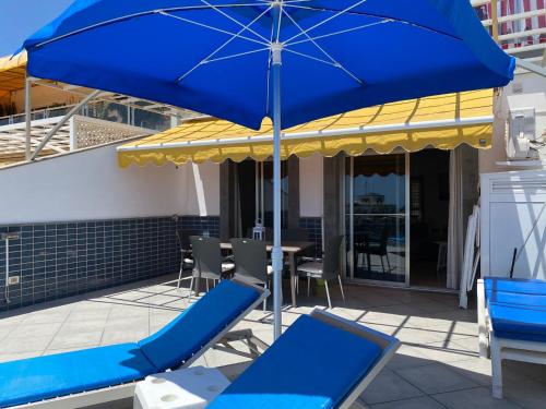 a blue umbrella and chairs on a patio at Billy's Beachfront Apartment with pool access in Puerto de Mogán