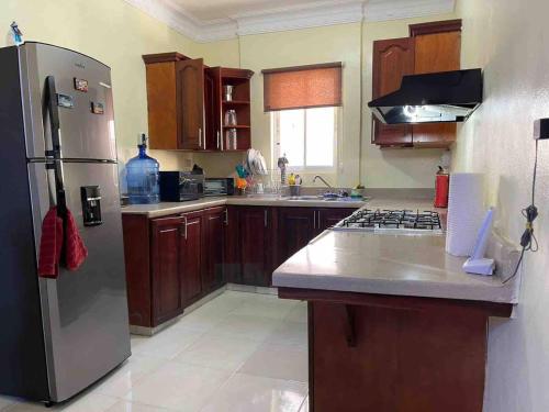 a kitchen with a stainless steel refrigerator and wooden cabinets at Entire Apartment Tu Nido De Amor netflix Wifi in Santo Domingo