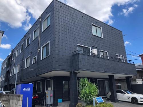 un edificio negro con un coche aparcado delante de él en Guest house ORCA, en Misato