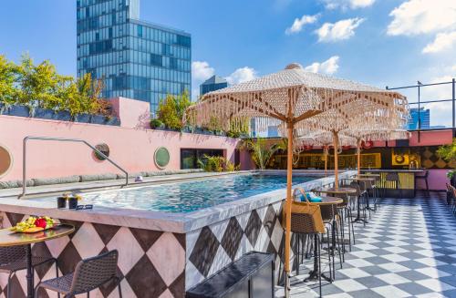 uma piscina exterior com mesas e cadeiras e um guarda-sol em Brown BoBo, a member of Brown Hotels em Tel Aviv