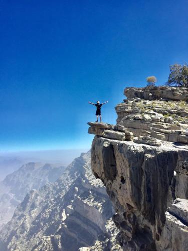 a man standing on the edge of a mountain at Canyon Rest House Jabal Shams in Al Ḩamrāʼ