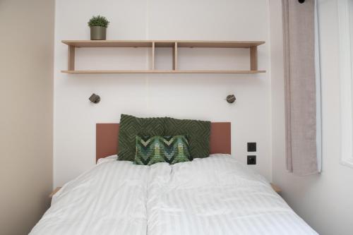 a bed with white sheets and green pillows on it at Tiny House in Enscherange
