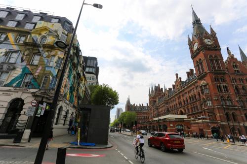 ロンドンにあるKX Rooms Kings Crossの時計塔と赤い車が並ぶ街道