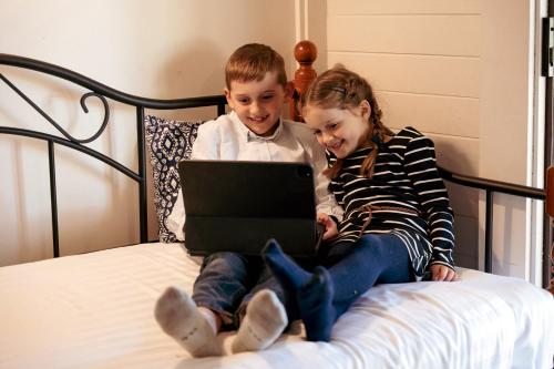 a boy and a girl sitting on a bed with a laptop at Hunter Valley Resort, Hunter Farm Adventure Centre & 4 Pines at the Farm in Pokolbin