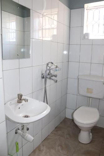a white bathroom with a toilet and a sink at Luwafu Guest House in Kampala
