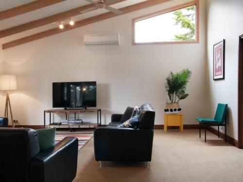 a living room with black furniture and a flat screen tv at Serena- a stone's throw from Lake Daylesford in Daylesford