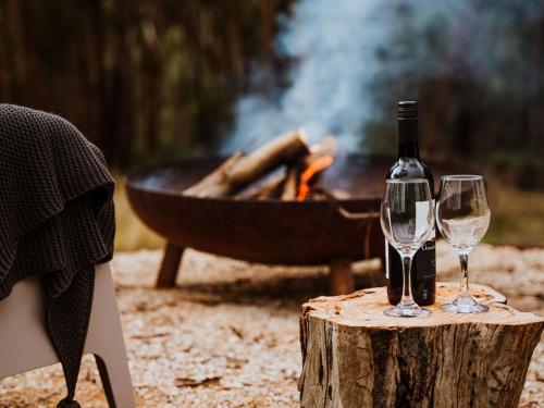 two wine glasses on a stump next to a grill at Lithic House -wood fire and bush views in Hepburn Springs