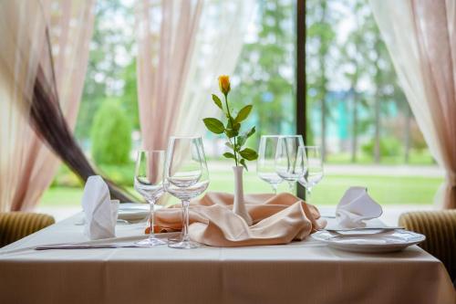 a table with glasses and a vase with a flower on it at Hotel Tigra in Priekuļi
