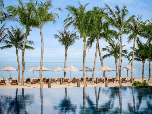 New World Phu Quoc Resort في فو كووك: حمام سباحة على الشاطئ مع أشجار النخيل والمظلات