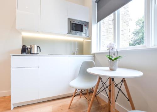 una cucina con armadi bianchi e tavolo bianco di Earls Court East Serviced Apartments by StayPrime a Londra