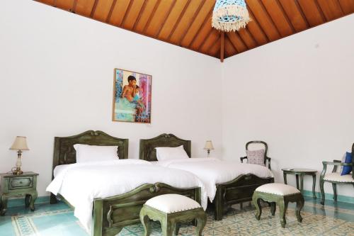 two beds in a white room with chairs and a chandelier at Bhumi Kasuryan Borobudur in Borobudur