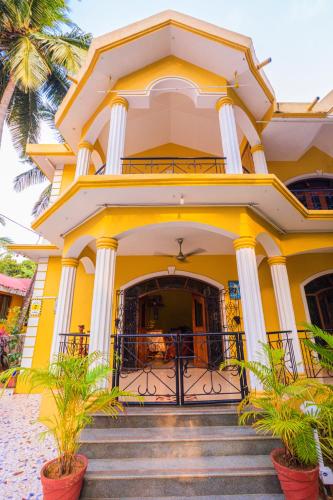 a yellow house with palm trees in front of it at Primavera Holiday Homes-FAMILY RUN GOAN GUEST HOUSE in Candolim