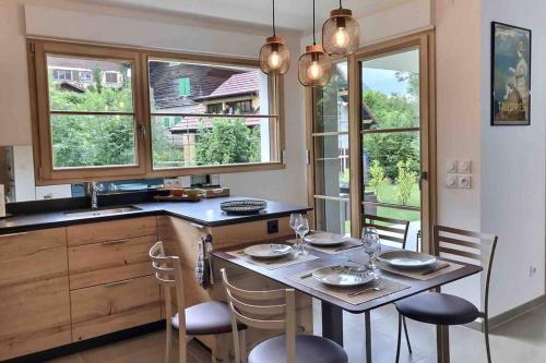 une cuisine avec une table, des chaises et des fenêtres dans l'établissement Très bel Appartement en rez de jardin, Talloires, à Talloires