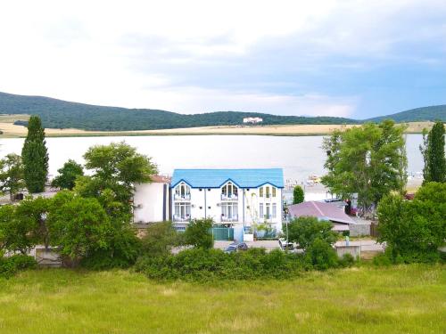 a large white house with a blue roof next to a lake at Laguna Beach Club Bazaleti Lake in Dushetʼi