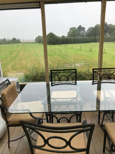 a glass table and chairs on a porch with a field at Leuk vakantiewoning dijk woning met 3 slaapkamers dicht bij de Belgische grensen in Westdorpe