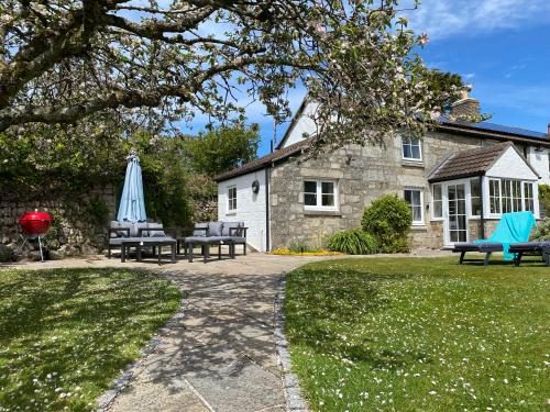 a patio with chairs and an umbrella and a house at Tresowes Green Cottage in Helston
