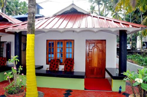 una pequeña casa con una puerta roja y sillas en Keratheeram Beach Resort, en Varkala