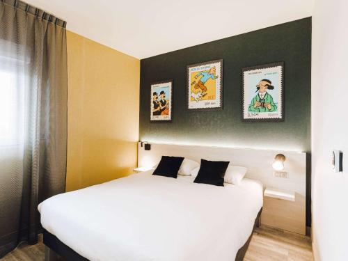 a hotel room with a large white bed and pictures on the wall at ibis Styles Contres-Cheverny in Le Controis En Sologne