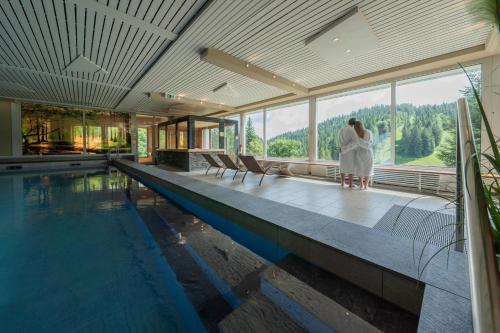 a couple standing next to a swimming pool in a house at Das Waldhotel - Genuss & Wellness am Notschreipass in Todtnau