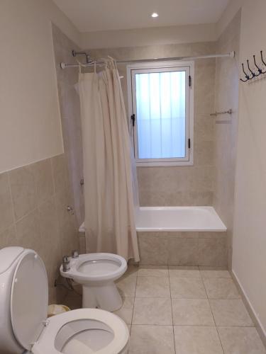 a bathroom with a toilet and a tub and a window at Pinamar Norte Casa Aquiles 8 pax in Pinamar