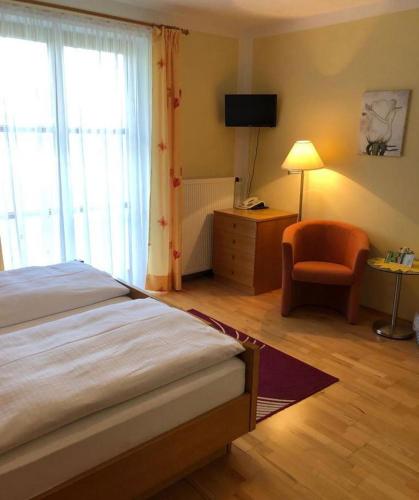 a bedroom with a bed and a chair and a window at Gästehaus Bauer am Golfplatz in Prien am Chiemsee