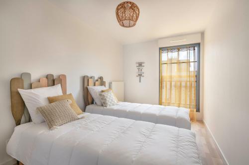 Duas camas num quarto branco com uma janela em Bel appartement pour 6 personnes avec balcon en bord de mer em Pléneuf-Val-André