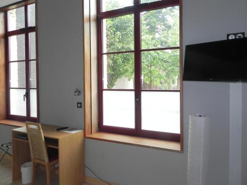 a room with three windows and a table and a desk with a television at Hôtel - Restaurant Au Tonnelier in Bergues
