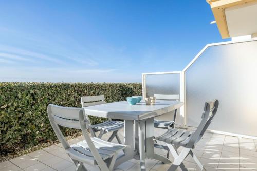 une table et des chaises blanches sur une terrasse avec une haie dans l'établissement À 200m de la plage, vue mer pour 4, au Croisic