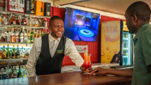 a man standing at a bar holding a drink at Kampi Ya Boma Kolwezi in Kolwezi