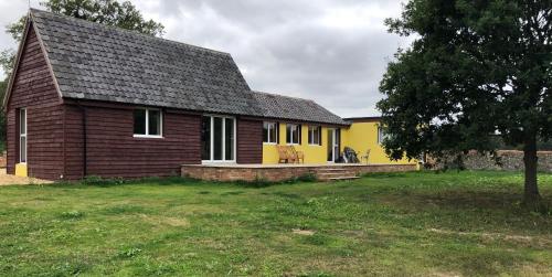 una pequeña casa amarilla y marrón con patio en Lower Farm Lodge en Stowmarket